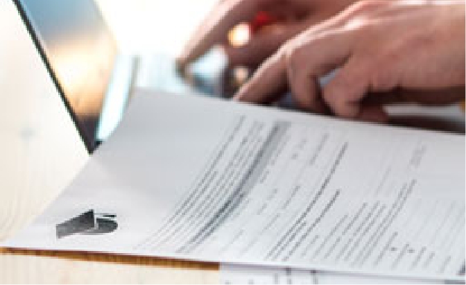 Hands typing on a laptop with a paper laying on the table