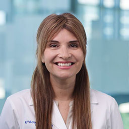 woman with long, brown hair wearing a white shirt and white coat with UT Southwestern Medical Center logo