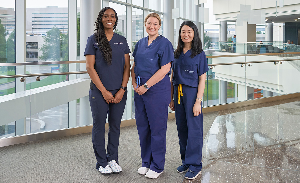 Three hospital employees posing in front of a large bay of windows.