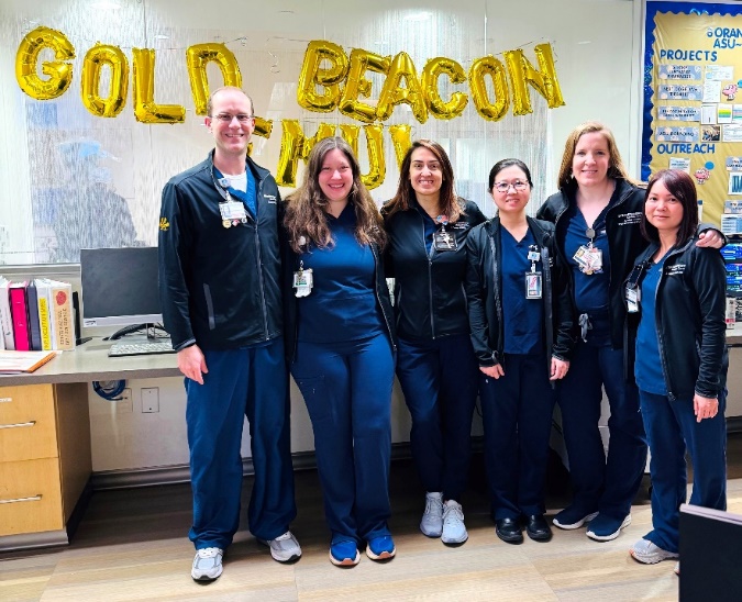 A small group photo in front of a Gold Beacon balloon banner