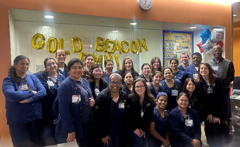 A large group photo in front of a Gold Beacon balloon banner