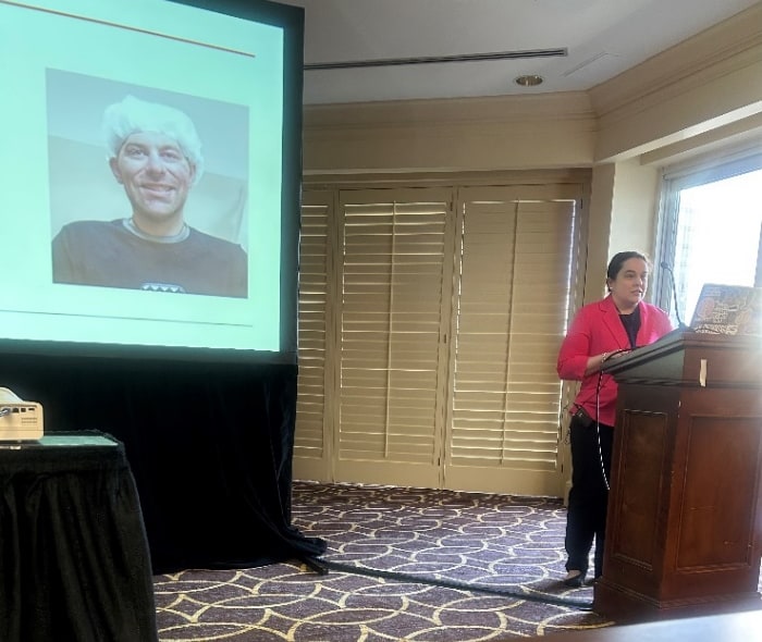 A woman speaks at a lectern with a projector screen behind her