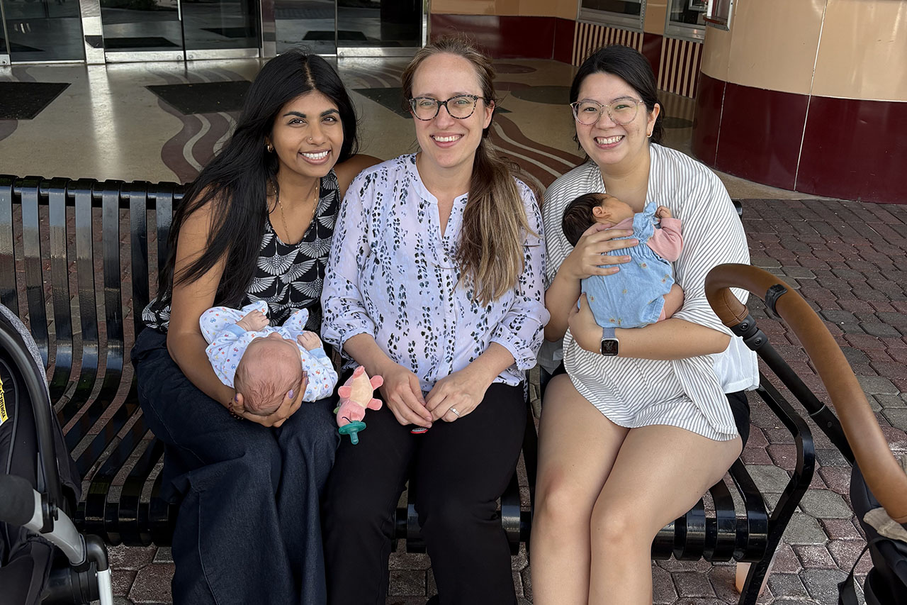 Three women sitting on a bench. Two of them are holding babies.