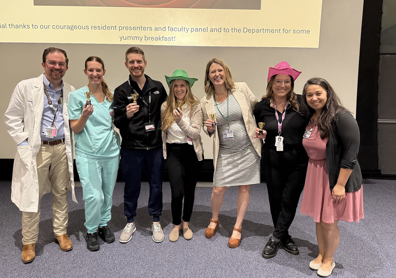 A group of residents and faculty hold small trophies and celebrate following a research presentation event.