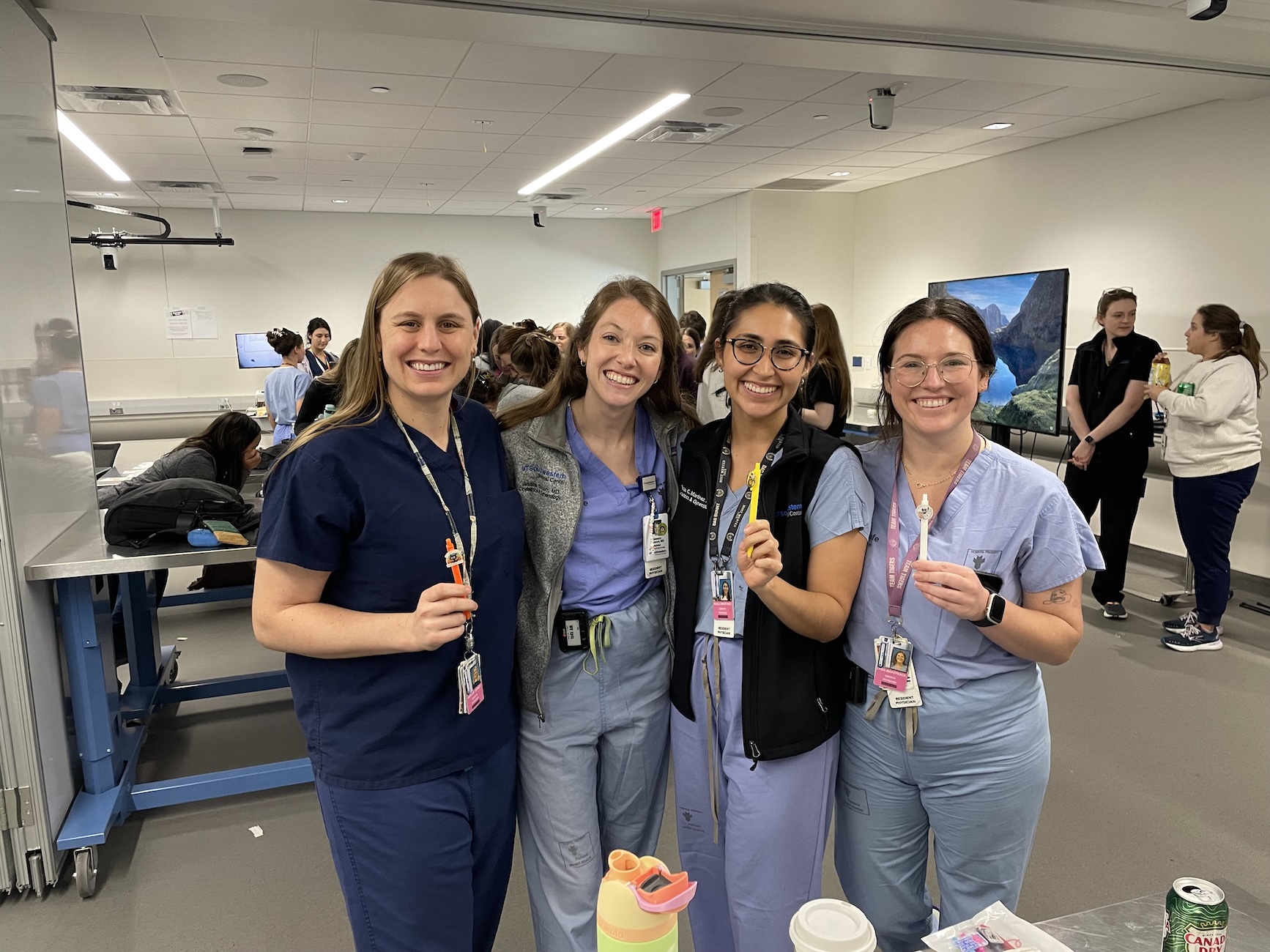 Four residents in scrubs smile together in a clinical training room.