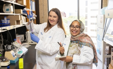 Two women in a lap wearing white lab coats smiling at the camera