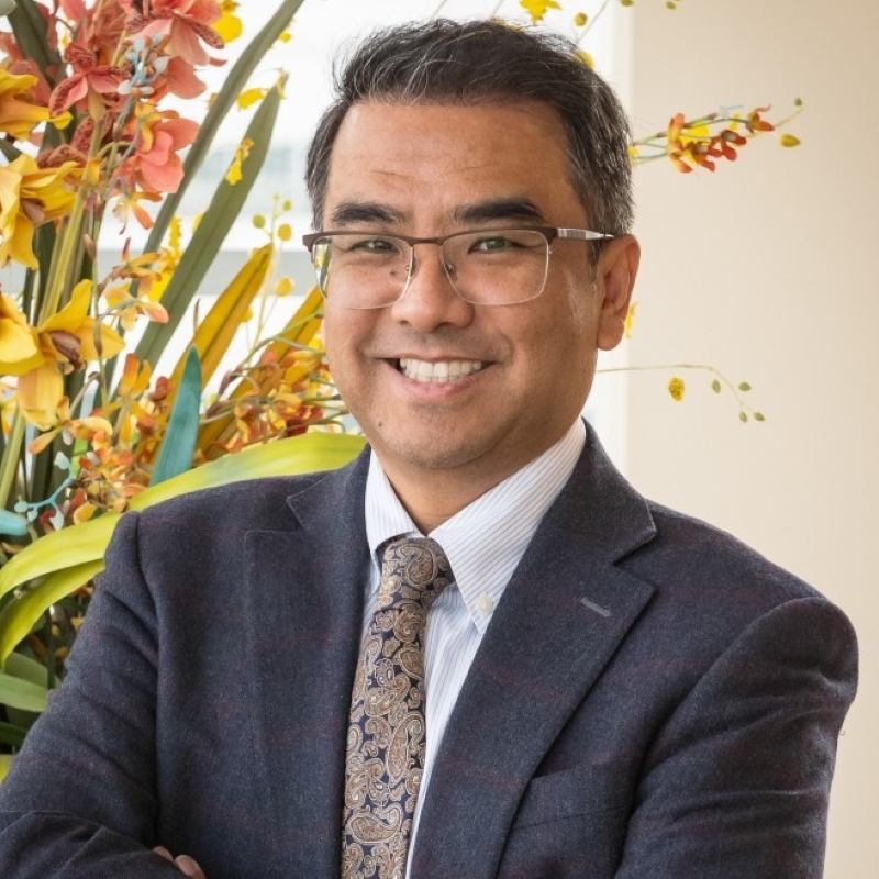 Dr. Zhang, a smiling man with dark hair, wearing a dark suit and glasses.