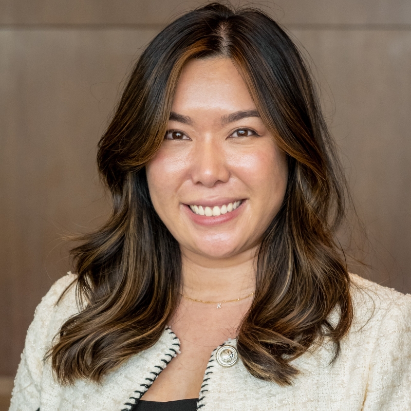 Dr. Huynh headshot, smiling woman with long dark hair in white jacket and dark shirt