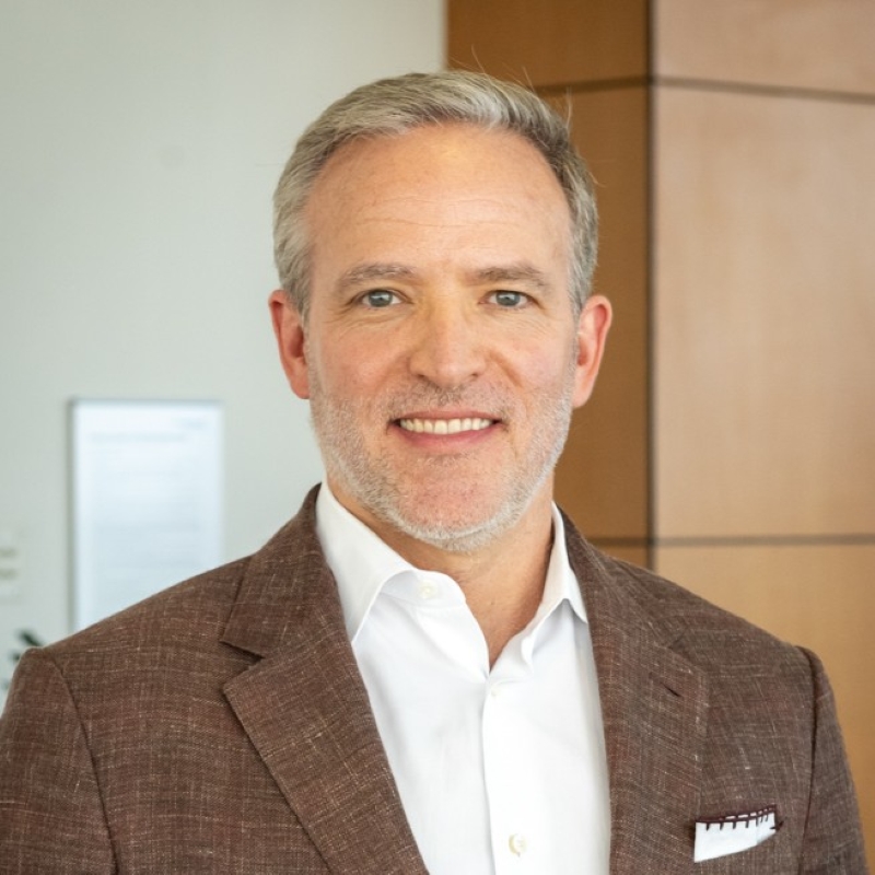 Dr. Haddock, a smiling man with blond hair, mustache and beard, wearing a dark suit over a plaid shirt with a salmon tie.