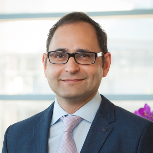 Dr. Teotia, a smiling man with dark hair and glasses, wearing a dark suit with a pink-checked tie.