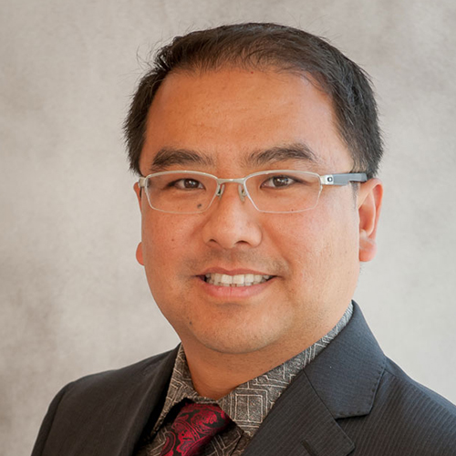 Dr. Zhang, a smiling man with dark hair, wearing a dark suit and glasses.