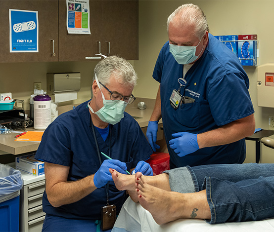 Two gloved and masked doctors performing wound care on a patient's foot.