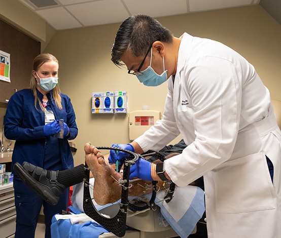 Doctor examining a patients foot wound while student observes.