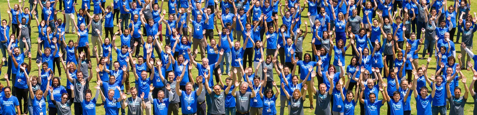 Members of the Simmons Comprehensive Cancer Center wearing blue or gray shirts wave while standing in a field