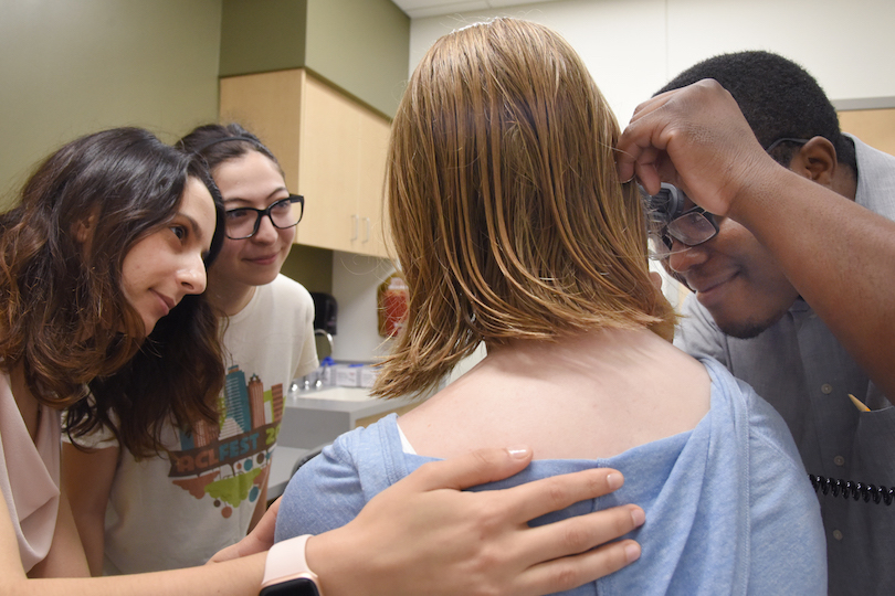 A male and two female students examine a female standardized patient's ear