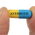 Two fingers holding a blue and yellow pill with the word Antibiotic