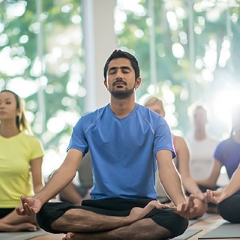 man in yoga class meditates with eyes closed while sitting in lotus position