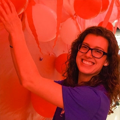 smiling young woman looks into camera while reaching up and holding red fabric sheet