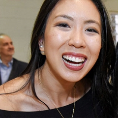 smiling woman looks into camera, wearing black top and gold chain necklace