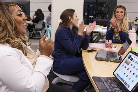 Three women clapping, sitting in front of laptops