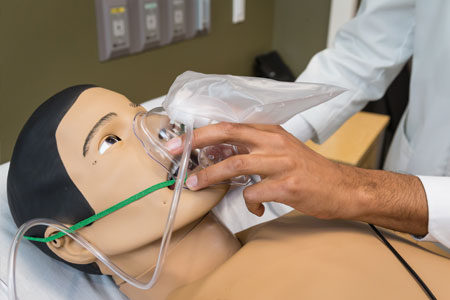 A hand holding breathing device on practice medical manikin face