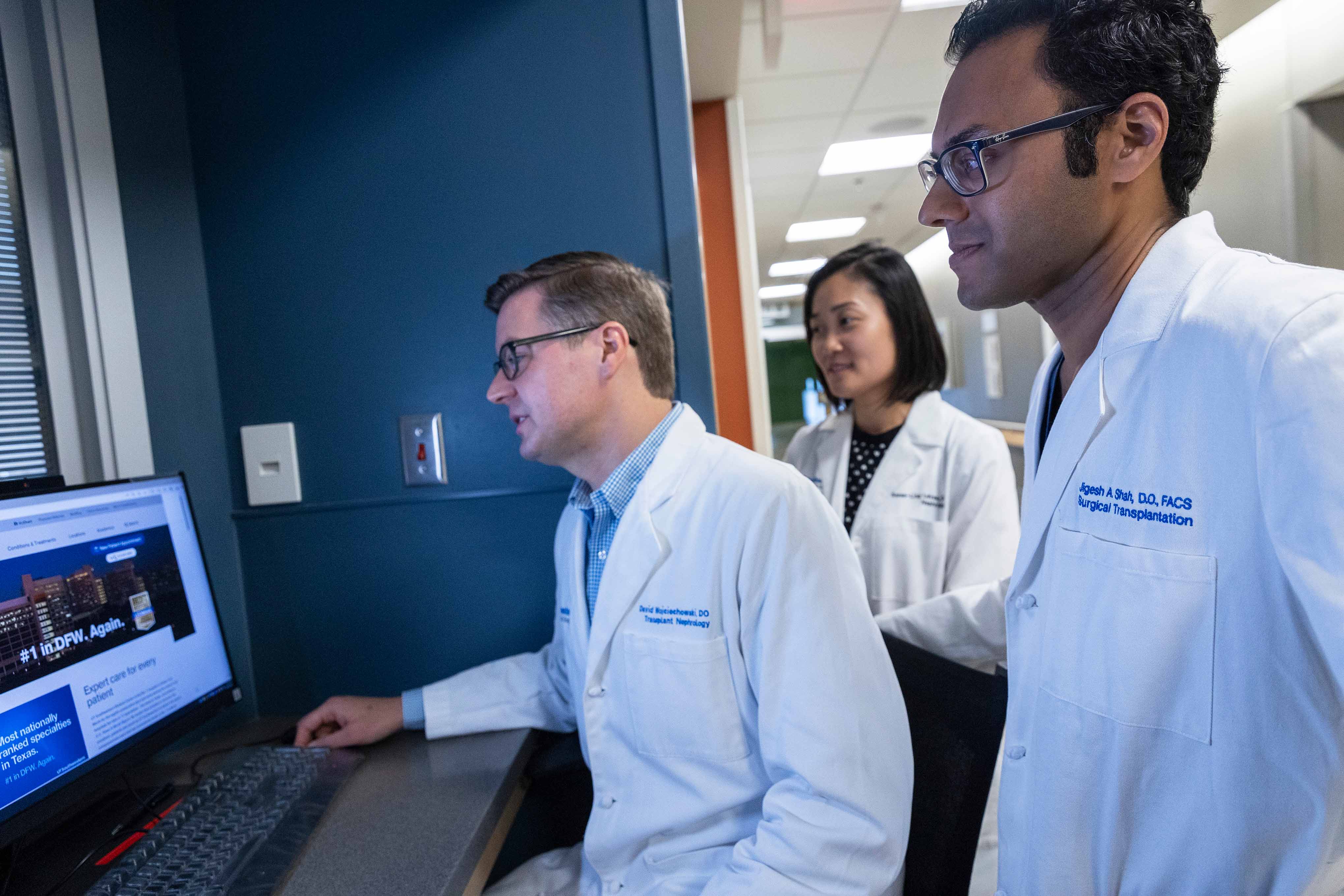 Two men in black scrubs and wearing PPE work at computers