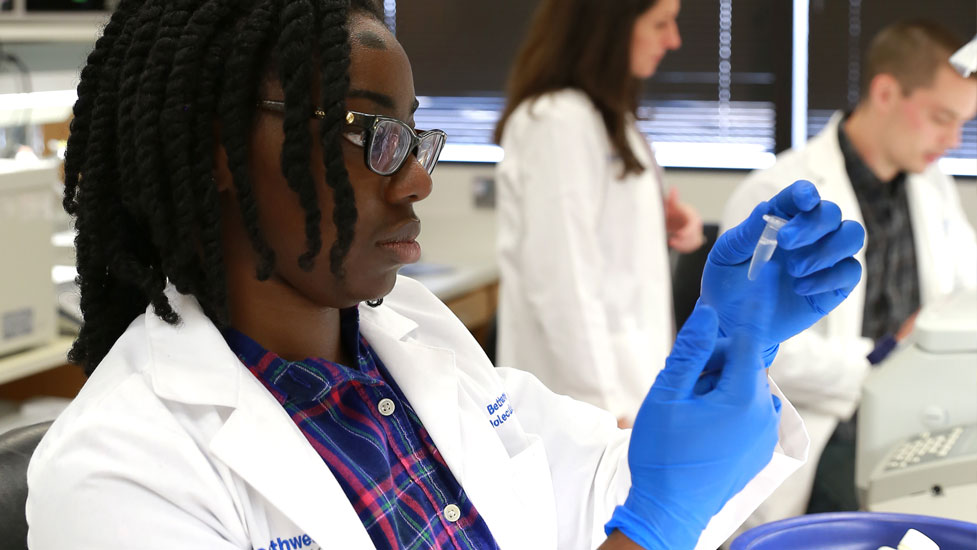 Student in lab looking at a sample in a vial