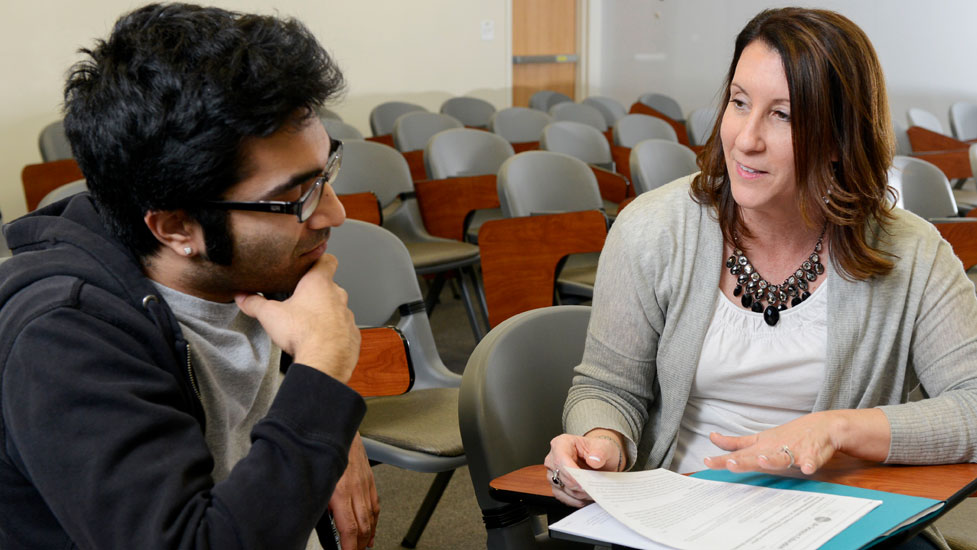 Two people reviewing and discussing documents in a classroom