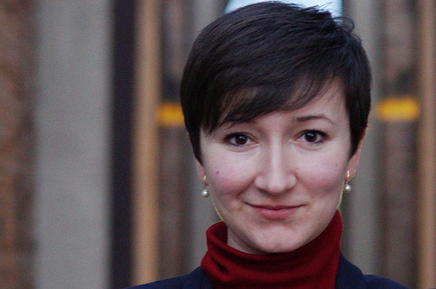 Woman with short dark hair, red turtle neck and blue blazer, arms crossed