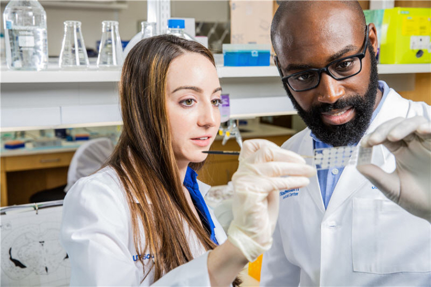 A white female researcher and a Black male researcher look at a slide