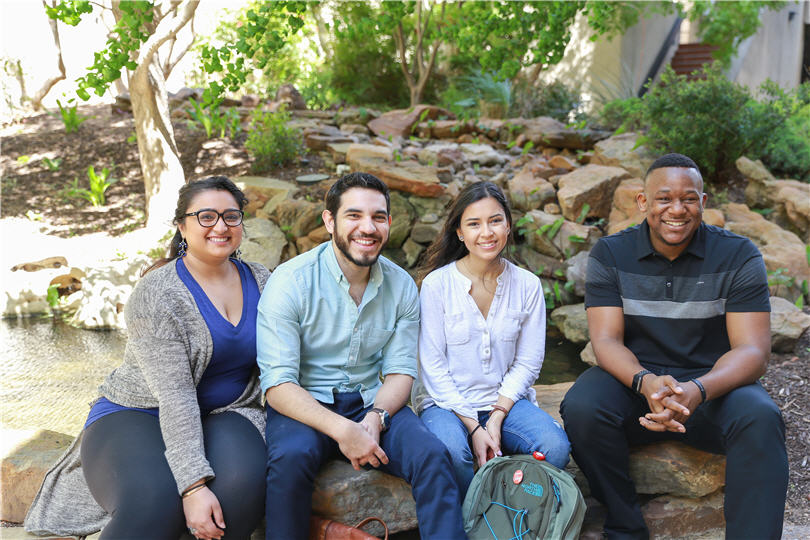 Two male and two female students sit in front of a rock garden