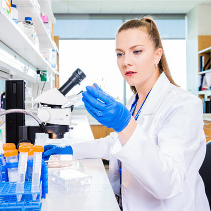 Woman in white coat and blue gloves stands at a microscope