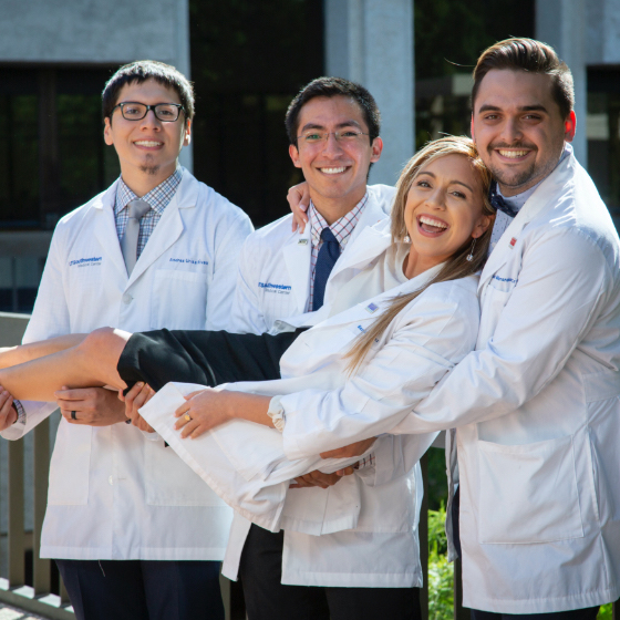 Three male medical students hold up a female medical student