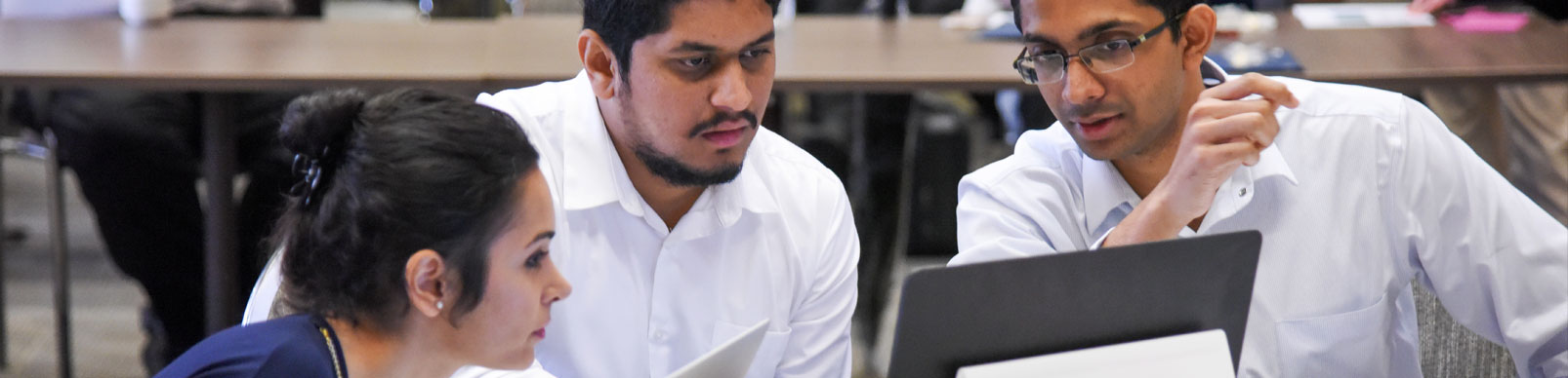 A woman and two men look at details on a laptop monitor