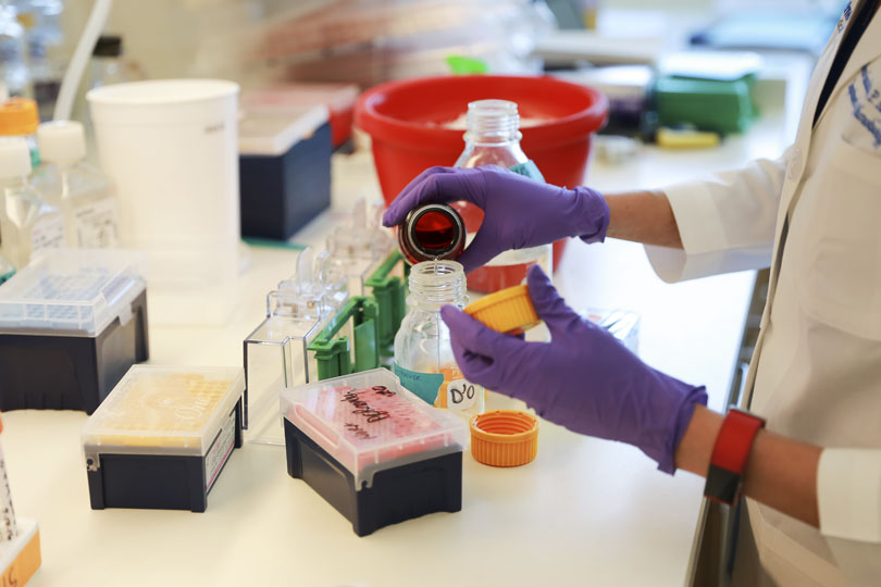 A researcher pours a clear liquid from a brown bottle into a clear bottle.