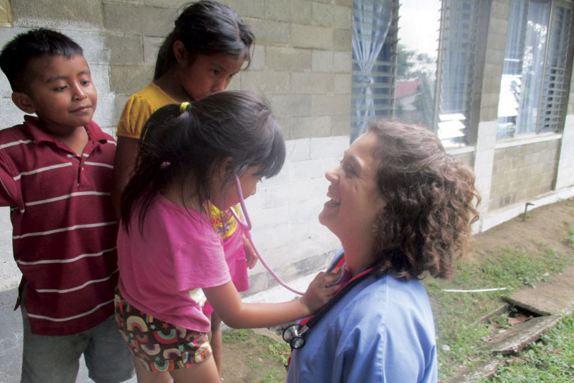 A young girl listens to a medical student's heart with a pink stethoscope.