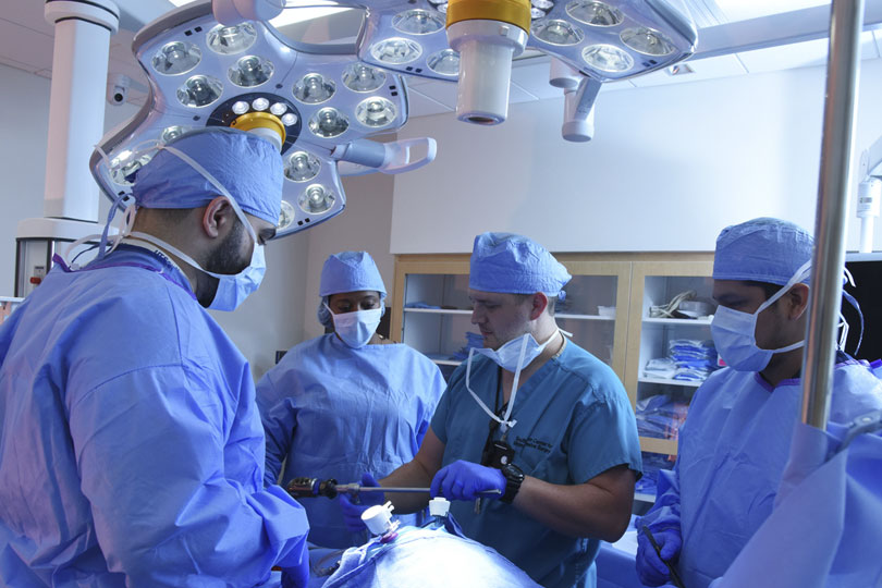 Students in masks and gowns practice surgery in the Simulation Center