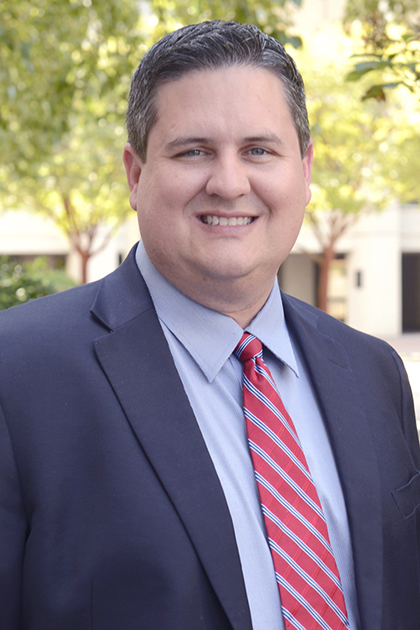 Cameron W. Slocum, a smiling man with brown hair wearing a dark suit, blue dress shirt, and red striped tie.