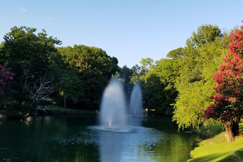 A fountain in a lake that is surrounded by green, yellow, and red trees