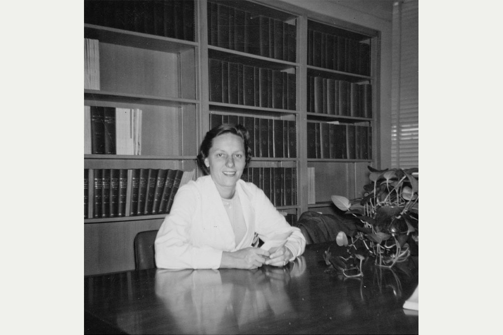 Peggy Whalley sits at a table in an office when she joined the faculty in 1961