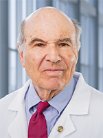 Distinguished balding man wearing a white lab coat over a blue shirt and burgundy tie.