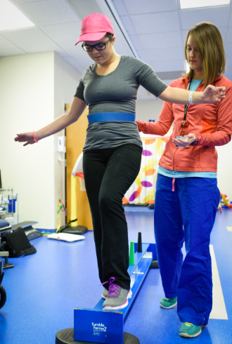 A female physical therapist assists a woman on a low balance beam