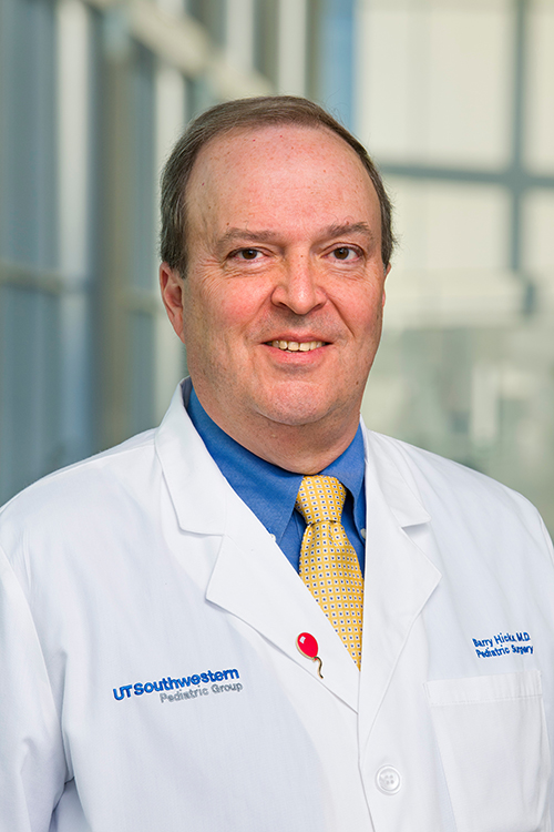 Barry Hicks, M.D., smiling man with medium brown hair, wearing a blue shirt and yellow tie beneath a lab coat.