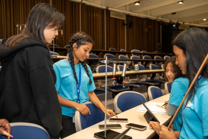 4 girls share notes on phones and tablets in lecture hall