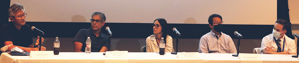 Five panel members seated at a long table listening as one member speaks