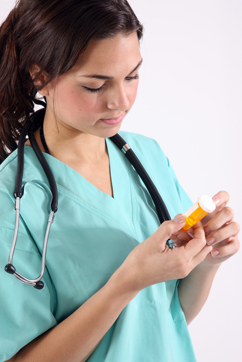 A woman in blue scrubs with a stethoscope around her neck looks at a pill bottle