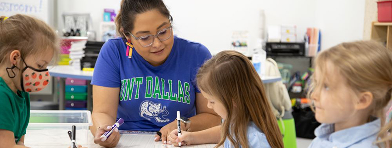 Three young female students working with female teacher at classroom table