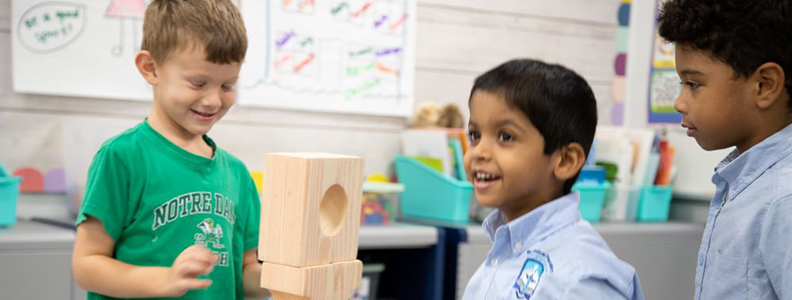 Three young male students working with large wooden blocks in classroom