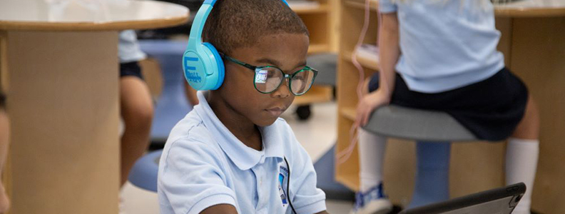 Young male student in classroom wearing headphones and using a laptop