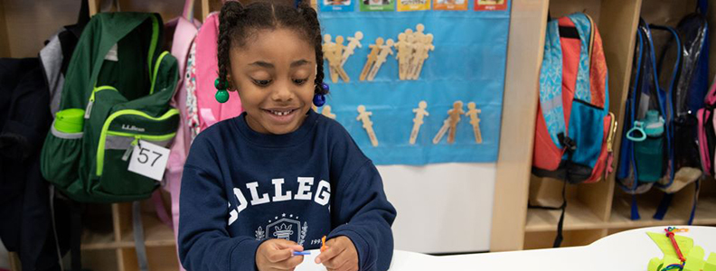 Young smiling female student works on a project at table in classroom